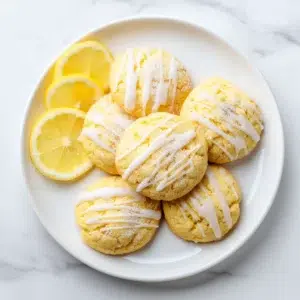 Lemon Cake Mix Cookies 5 Lemon cake mix cookies arranged on a white plate with lemon glaze drizzle, bright natural light