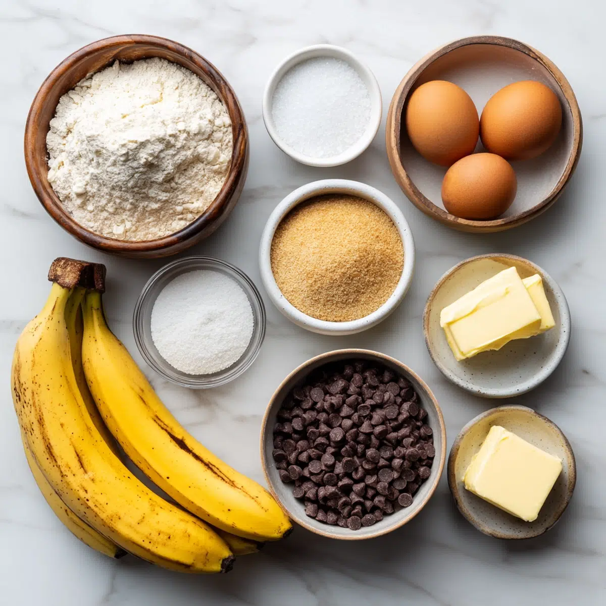 healthy banana chocolate chip bread ingredients flat-lay with ripe bananas, butter, eggs, flour, and chocolate chips